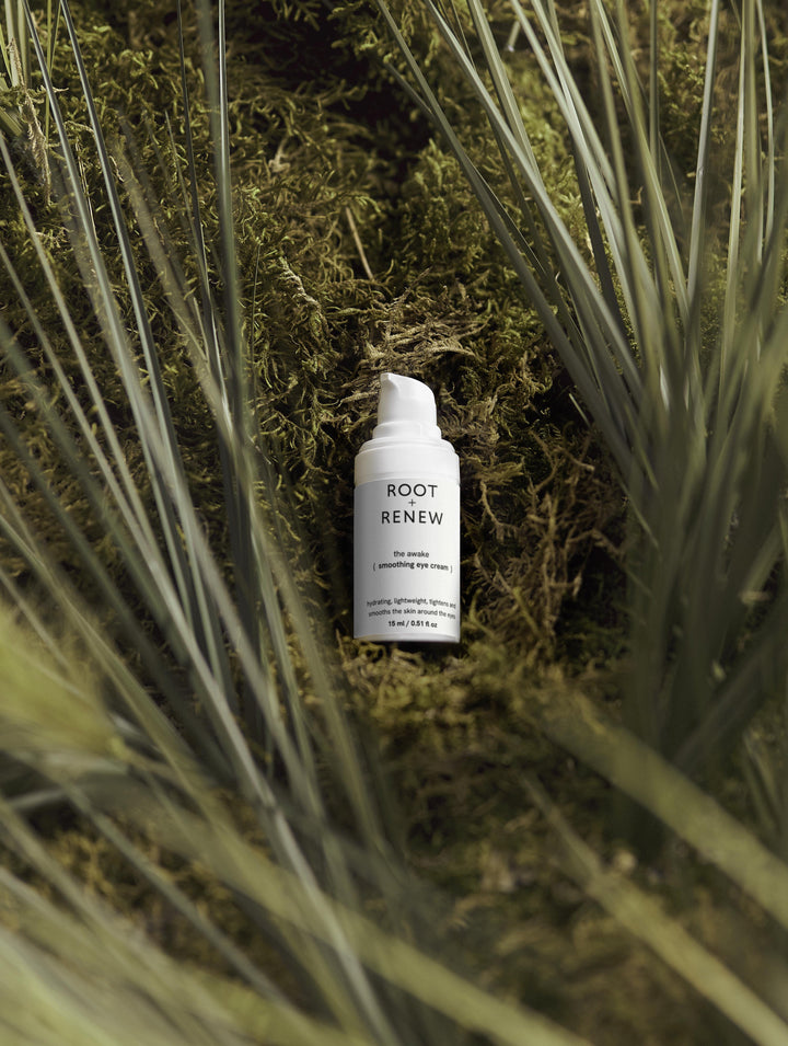 Root + Renew’s The Awake Eye Cream nestled in soft green moss and surrounded by tall grass, capturing a serene, botanical vibe.

