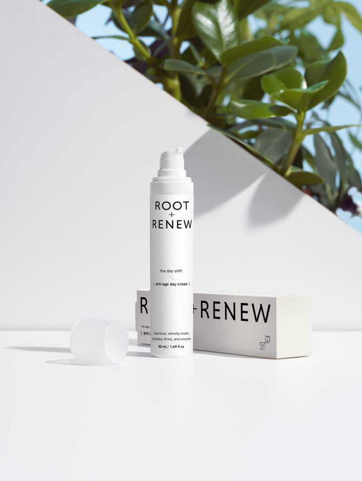 Root + Renew The Day Shift anti-age cream with cap and box on white surface, styled with natural sunlight and leafy background

